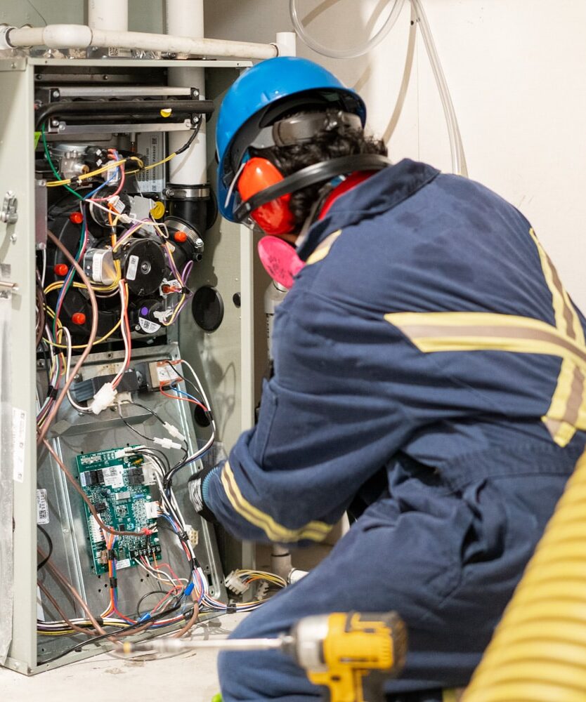 An Alberta Furnace Cleaning technician in a clean, sharp uniform looking at the wiring of a furnace.