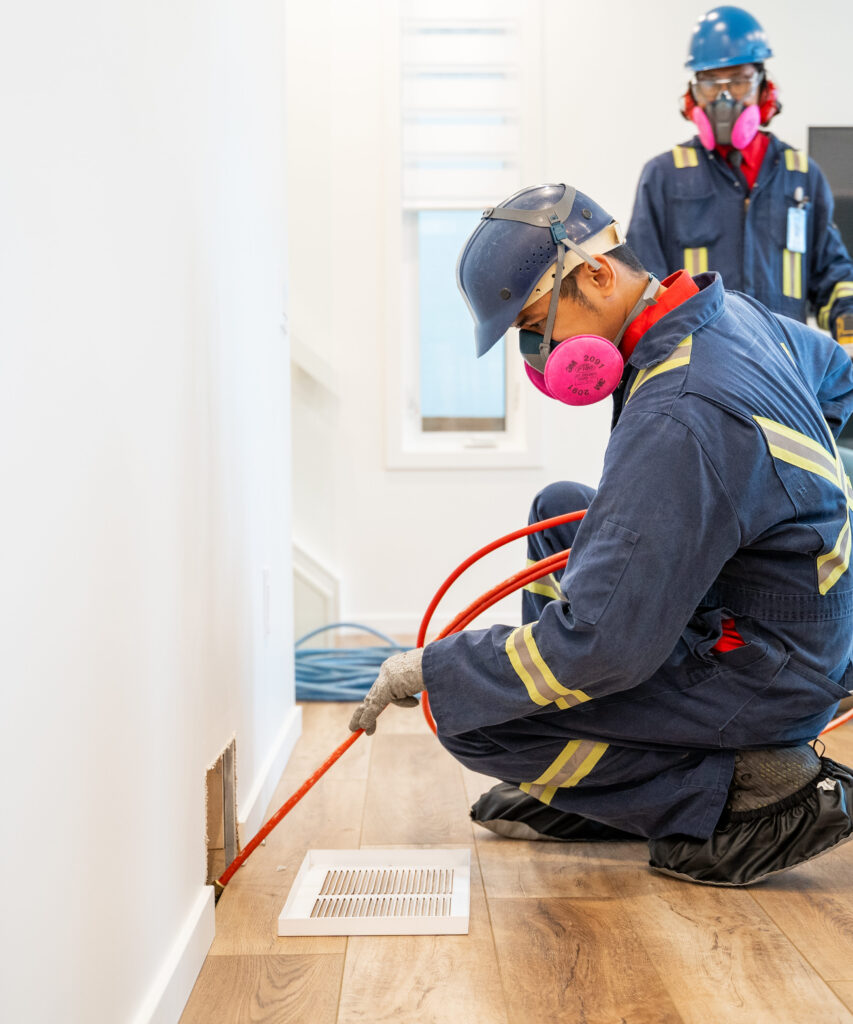 An Alberta Furnace Cleaning technician in a clean, sharp uniform looking cleaning the duct in a customers' home. 