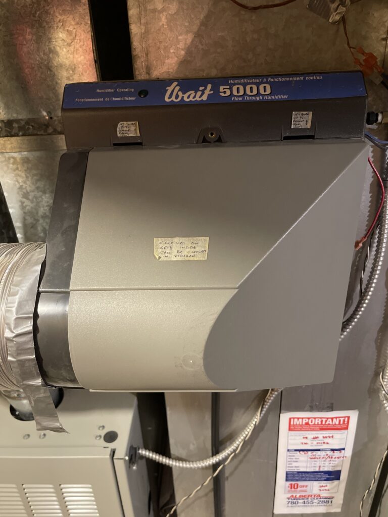 A picture of a flow through humidifier attached to ductwork above a furnace.