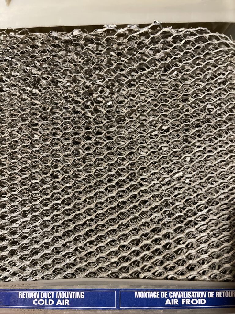 A close up of a wire humidifier pad in a flow through humidifier with the words "return duct mounting cold air" below it.